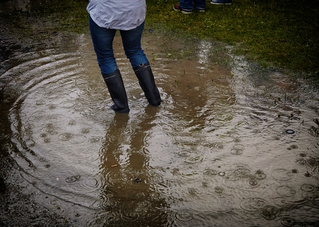 Person in rainboots splashing in a puddle in a yard in need of a drainage system installation